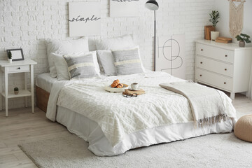 Interior of light bedroom with lamp, breakfast and books on bed