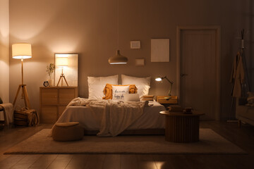 Interior of dark bedroom with glowing lamps, laptop and books on bed at night