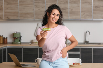 African-American woman with tasty eclair in kitchen