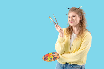 Female artist with paint brushes and palette on blue background
