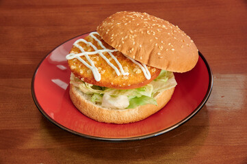 A hamburger with lettuce and mayonnaise on a red plate. The bun is brown and the lettuce is green