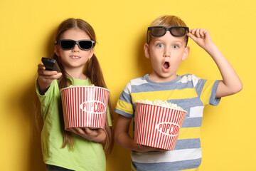 Fototapeta premium Little children in 3D glasses with popcorn watching TV on yellow background