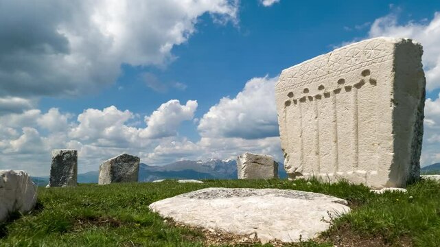 Tombstone (stećak) in ancient graveyard - stećci in medieval cemetery time lapse - historical carved stone with decoration by a grave (tomb) under dramatic sky with fast moving clouds.