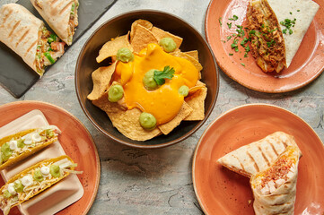 A table is filled with a variety of Mexican dishes such as burritos, tacos, and nachos. There are several bowls and plates with different types of food, including a bowl of nachos with guacamole