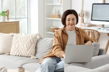 Fototapeta premium Mature woman using laptop on sofa at home