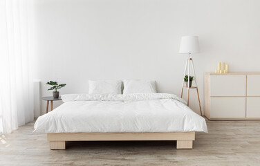 Real photo of bedroom interior in simple style. Big bed with pillows, wooden floor, window with...