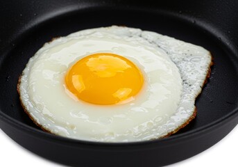 Fried Egg in Black Pan Isolated on White - A single fried egg with a runny yolk sits in a black pan against a pristine white background. This symbolizes simplicity, breakfast, nourishment, health