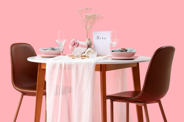 Restaurant table for two with plates, flowers and heart-shaped gift box on pink background