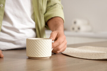 Young man with ceramic cup on table in kitchen, closeup