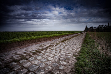 Cobblestone road stretching through rural landscape. Key cobbled sector of the famous " Paris-Roubaix "  cycling race classics.