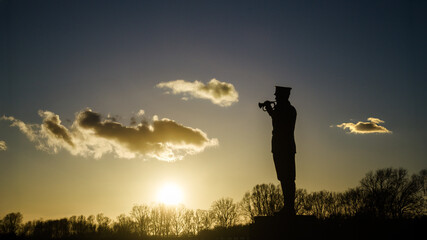 Silhouette of a military trumpet player statue against a sunset sky. Memorial of World War One in...
