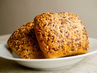 Three crusty rolls with seeds and grain in white bowl on simple light color table cloth. Fine bakery product made from high quality ingredients, Small bread.