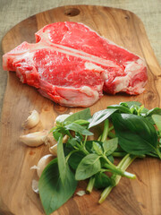 Luxurious T bone steak on a wooden cutting board with garlic and fresh green basil herb. Expensive high quality raw meat product with fantastic flavor. Top quality beef.