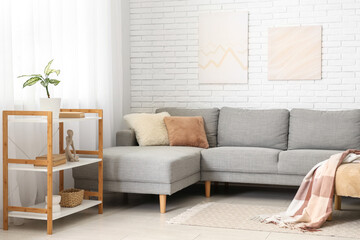 Interior of light living room with grey sofa and shelving unit near white brick wall