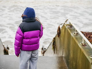 Teenager girl looking at powerful ocean waves on a windy day. Travel and tourism concept. Model is...