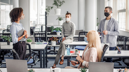 Report on work, meeting or team building during covid-19 outbreak and social distancing. Young african american lady with tablet speaks to colleagues in modern office interior with gadgets, panorama