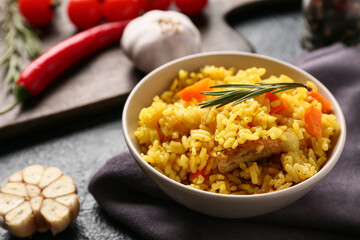 Bowl with tasty pilaf and ingredients on dark background