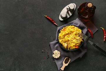 Bowl of tasty pilaf with chili peppers and garlic on black background