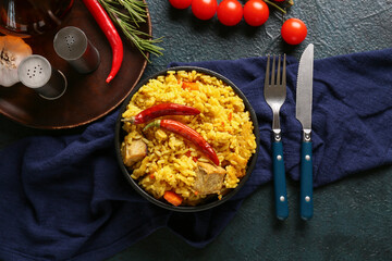 Bowl with tasty pilaf and ingredients on dark background