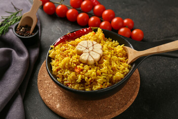 Frying pan of tasty pilaf with garlic, chili pepper and cherry tomatoes on black background, closeup