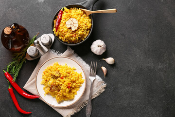 Plate and bowl of tasty pilaf with ingredients on black background