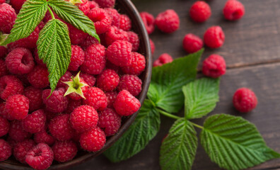 Raspberries closeup on rustic wood background. Bowl with natural ripe organic berries with peduncles and green leaves on wooden table, top view