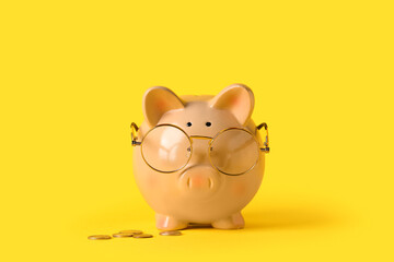 Piggy bank with eyeglasses and coins on yellow background