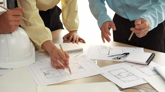 Smart architect and safety engineer discussion about building blueprint on table with architectural document, measurement tools and wooden block scatter around at modern office. Closeup. Delineation.