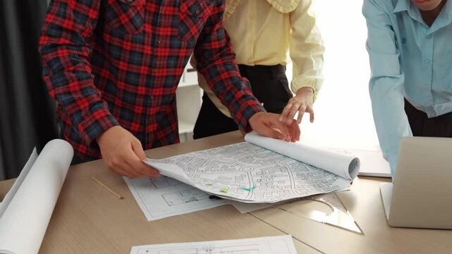Professional engineer team discussion about house design on meeting table with architectural equipment and building blueprint scatter around at modern office. Focus on hand. Closeup. Delineation.