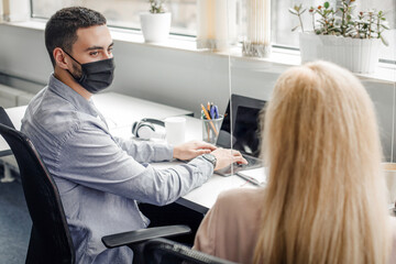 Modern workplace in coworking office after covid quarantine. Guy and lady in protective masks...