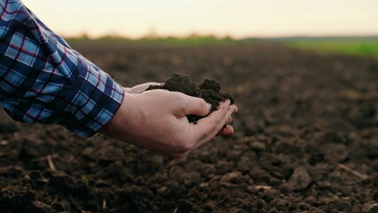 Male hands hold fertile land in field. Organic soil in hands of farmer at sunset in field, natural...