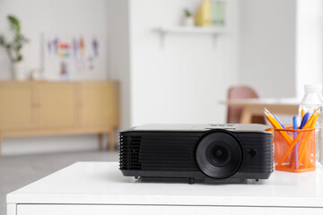 Modern projector with pencil cup and water bottle on designer's table in office, closeup
