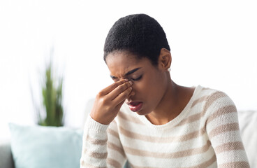 Sinusitis Concept. Sick Young Black Woman Touching Her Nose Bridge While Sitting On Couch At Home,...