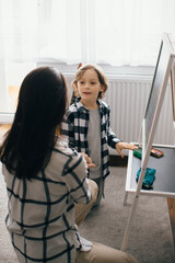 Mother kneeling and interacting with son at home by blackboard