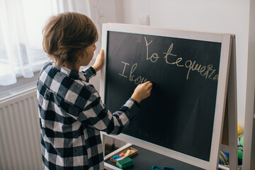 Child writing on blackboard at home: learning spanish