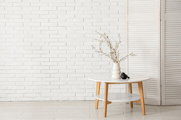 Folding screen and blooming tree branches on coffee table near white brick wall