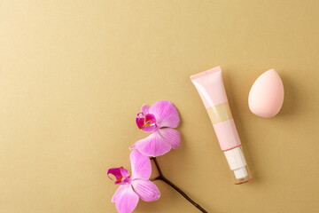 Cosmetic foundation tube with pink orchid and beauty sponge on neutral background. Top view, flat...