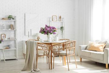 Interior of room with dining table, sofa and lilac flowers in vase