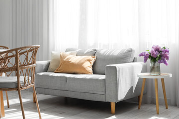 Interior of light room with sofa and lilac flowers in vase