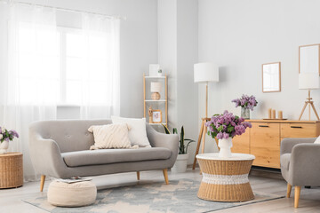 Interior of light living room with sofa, armchair and lilac flowers in vases