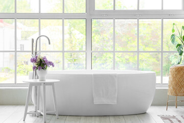 Vase with lilac flowers on table near bathtub in room