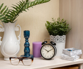 A white vase with a blue candle and a clock on a shelf