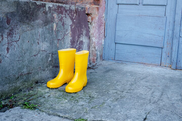 Two yellow rain boots are standing on a concrete sidewalk