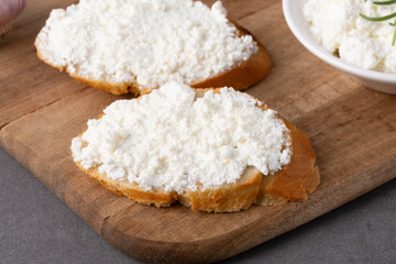 Slices of bread are spread with cream cheese and placed on a rustic wooden board.