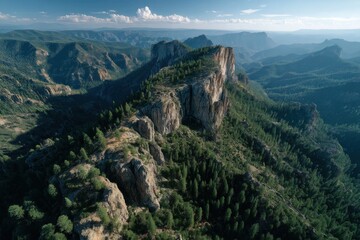 Aerial view of a rocky peak covered with dense forest, rugged cliffs, and mountainous landscapes under a clear blue sky