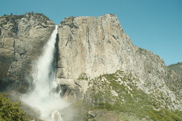 Scenery with granite cliffs, greenery, cascading waterfalls blue skies at Yosemite National Park in California’s Sierra Nevada mountains