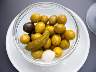 Perfect addition to meat and fish dishes - pickled fruits and vegetables. Bowl contains traditional Spanish snack - canned olives, onions, cucumbers.