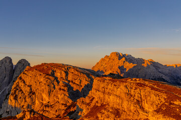 Sunset silhouettes of the mountains in the Dolomites Alps. Beautiful landscape of the rocky cliffs in Dolomiti Alps at sunset and sunrise light with some clouds red, orange and yellow color of sky
