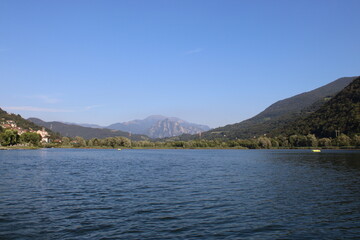Fototapeta premium On Lake Endine, the calm water reflects the blue sky. Green mountains surround the valley, with small villages along the shores and lush nature that creates an atmosphere of peace and serenity.