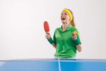 Joyful female athlete in green sportswear and yellow headband celebrates win in a table tennis...